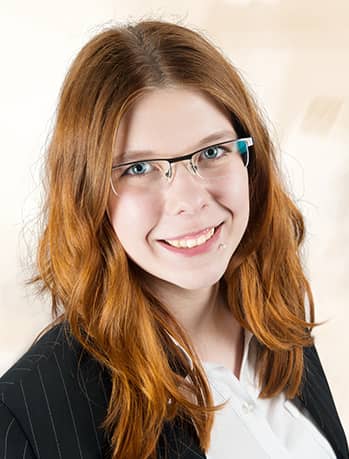 Frau mit neutralem Blick, roten Wellenhaaren, schwarzem Nadelstreifenblazer
